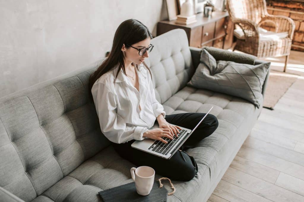 Woman researching a car finance calculator on a laptop while sitting on a sofa at home – budgeting and planning for a new car purchase in the UK